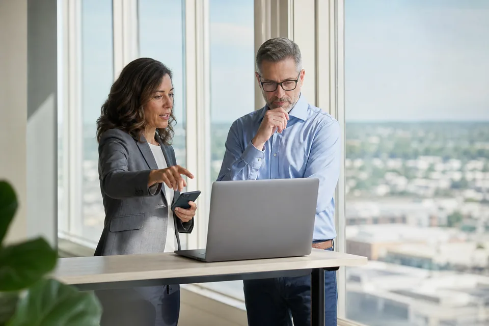 Two IT managers in an office discussing which uptime monitoring vendor to choose, one holding a phone